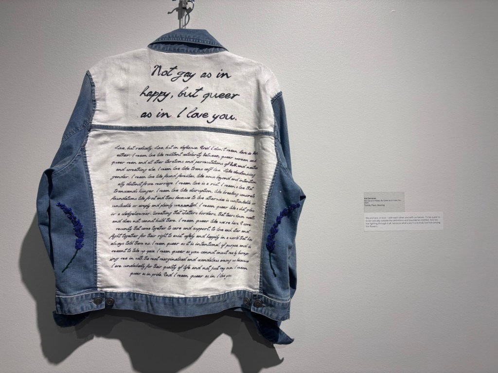 Blue and white jacket hanging in front of a white wall with spotlight lighting. The back panels of the jacket (which are facing toward the camera) are painted white, with black lettering.