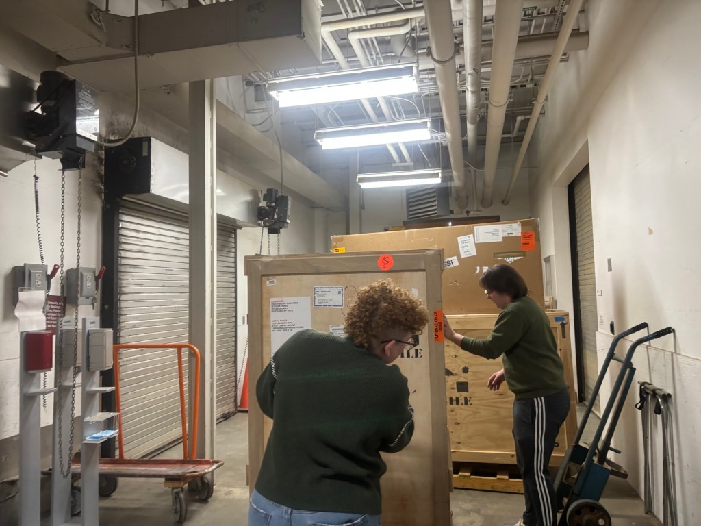 Two people wheeling large crates in a loading dock space. 