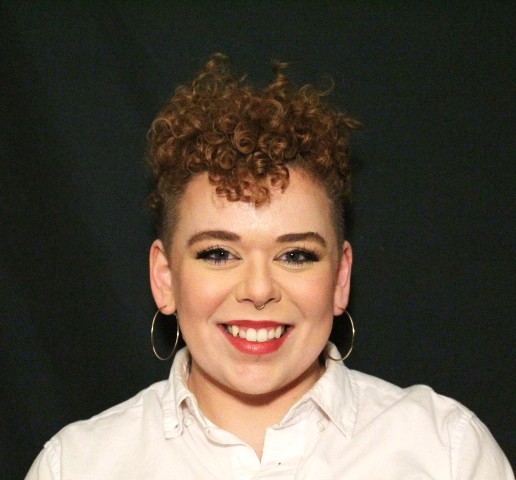 Headshot of Kal Demaree (pale, short red curly hair, in white button up shirt) in front of a dark green background. 